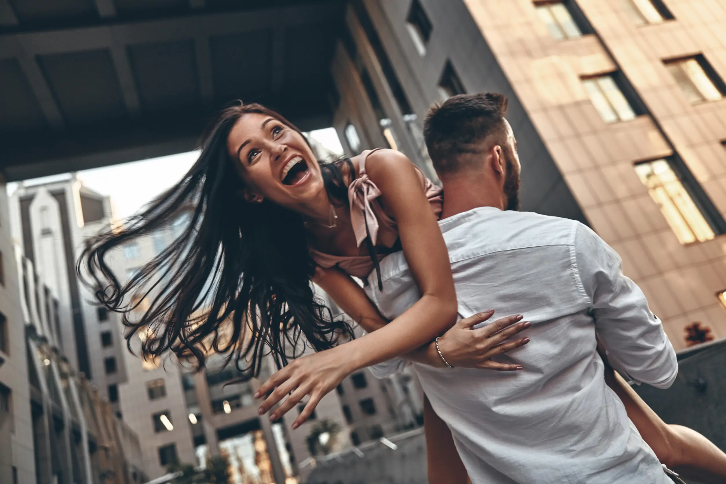 Feeling playful. Beautiful young woman keeping mouth open while her boyfriend carrying her outdoors